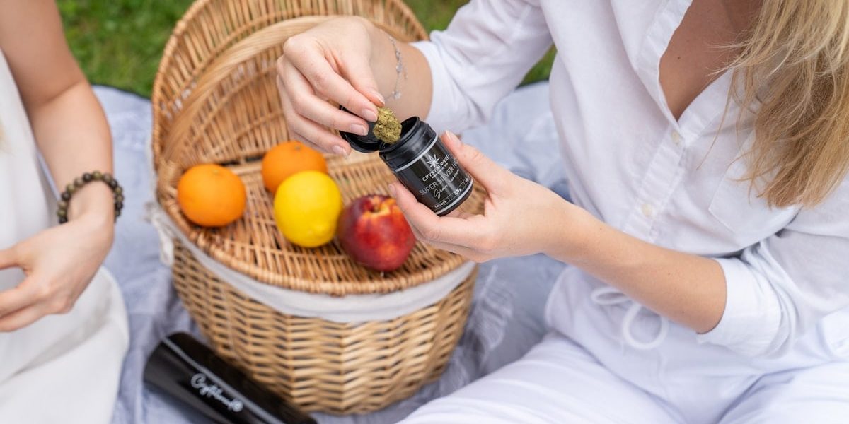 two women sitting on the grass with a basket of fruit